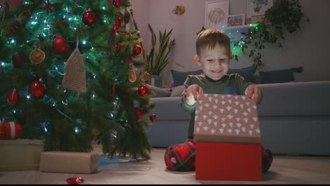 Ein-Glücklich-Lächelnder-Kleiner-Junge-öffnet-Sein-Weihnachtsgeschenk-Vom-Weihnachtsmann.-Junge-öffnet-Weihnachtsgeschenk-Zu-Hause.-Hochwertiges-4K-Filmmaterial